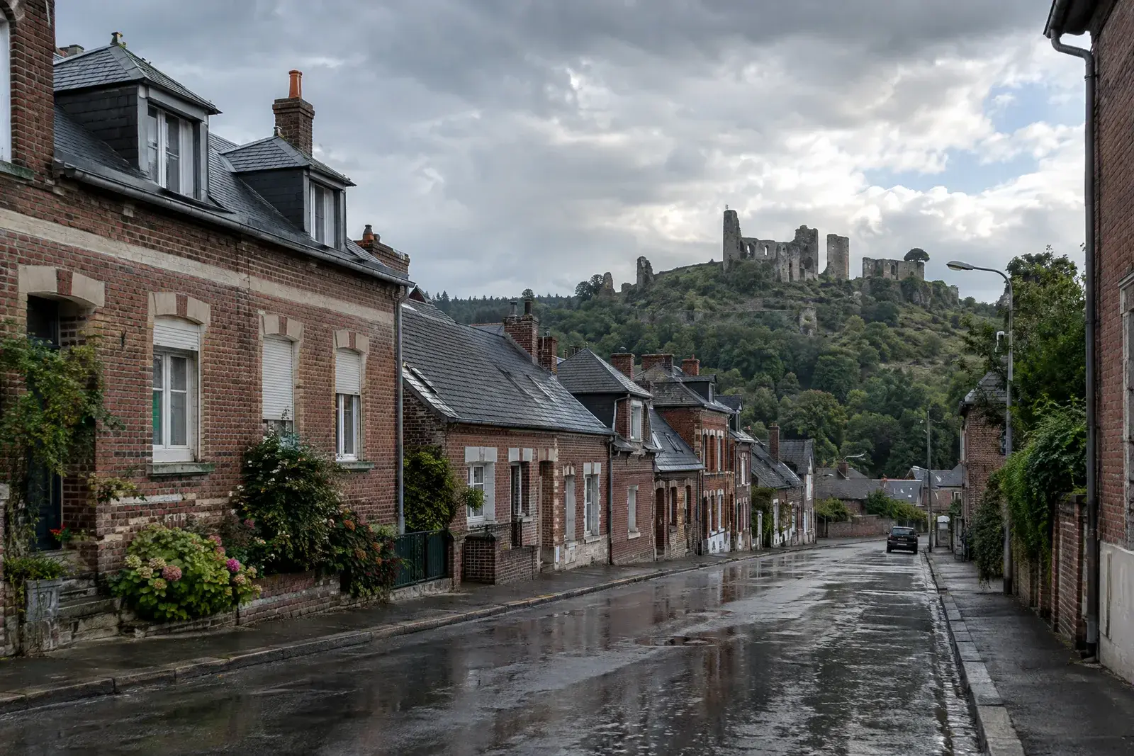 Rue de maisons de brique aux toits d’ardoise après la pluie, ruines d’un château fort sur la colline boisée