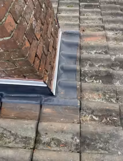 Solin neuf posé au pied d’une souche de cheminée en brique, sur une toiture en tuiles