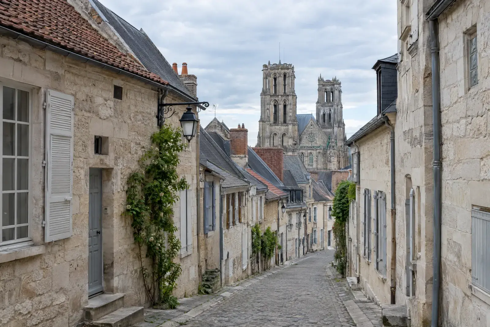 Ruelle d’une ville haute ancienne, maisons de pierre aux toits de tuile plate et d’ardoise, tours d’une cathédrale gothique au fond